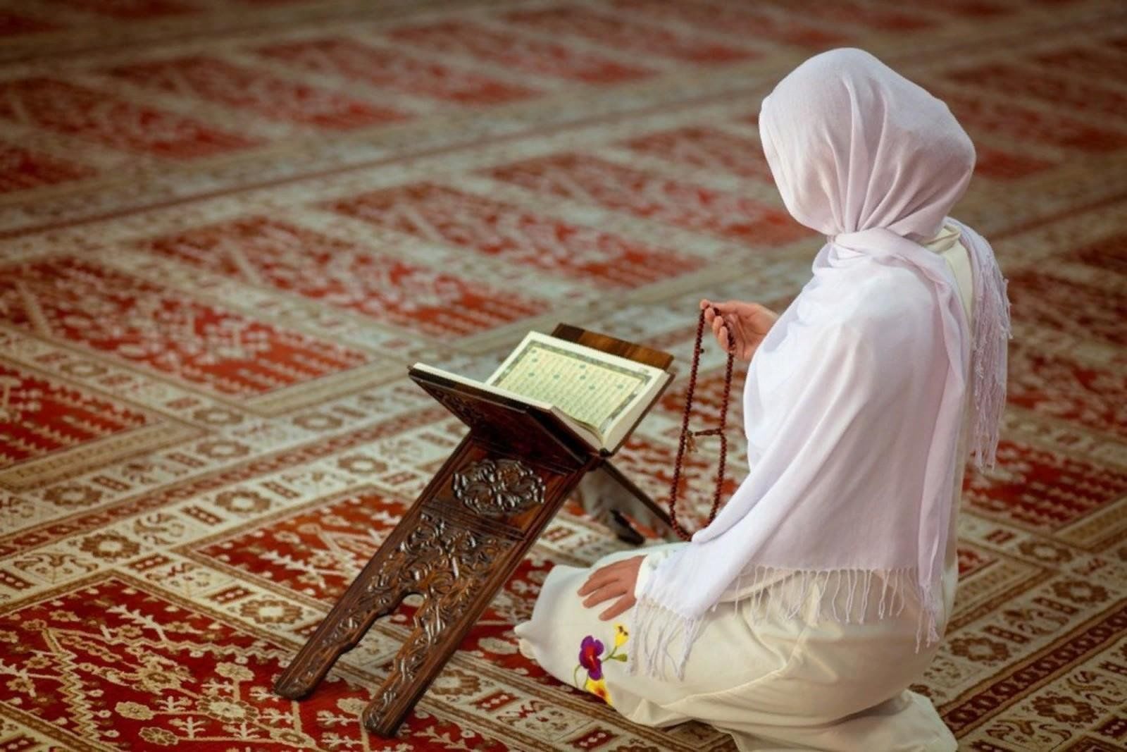 Молодая мусульманская женщина моля в мечети с Кораном