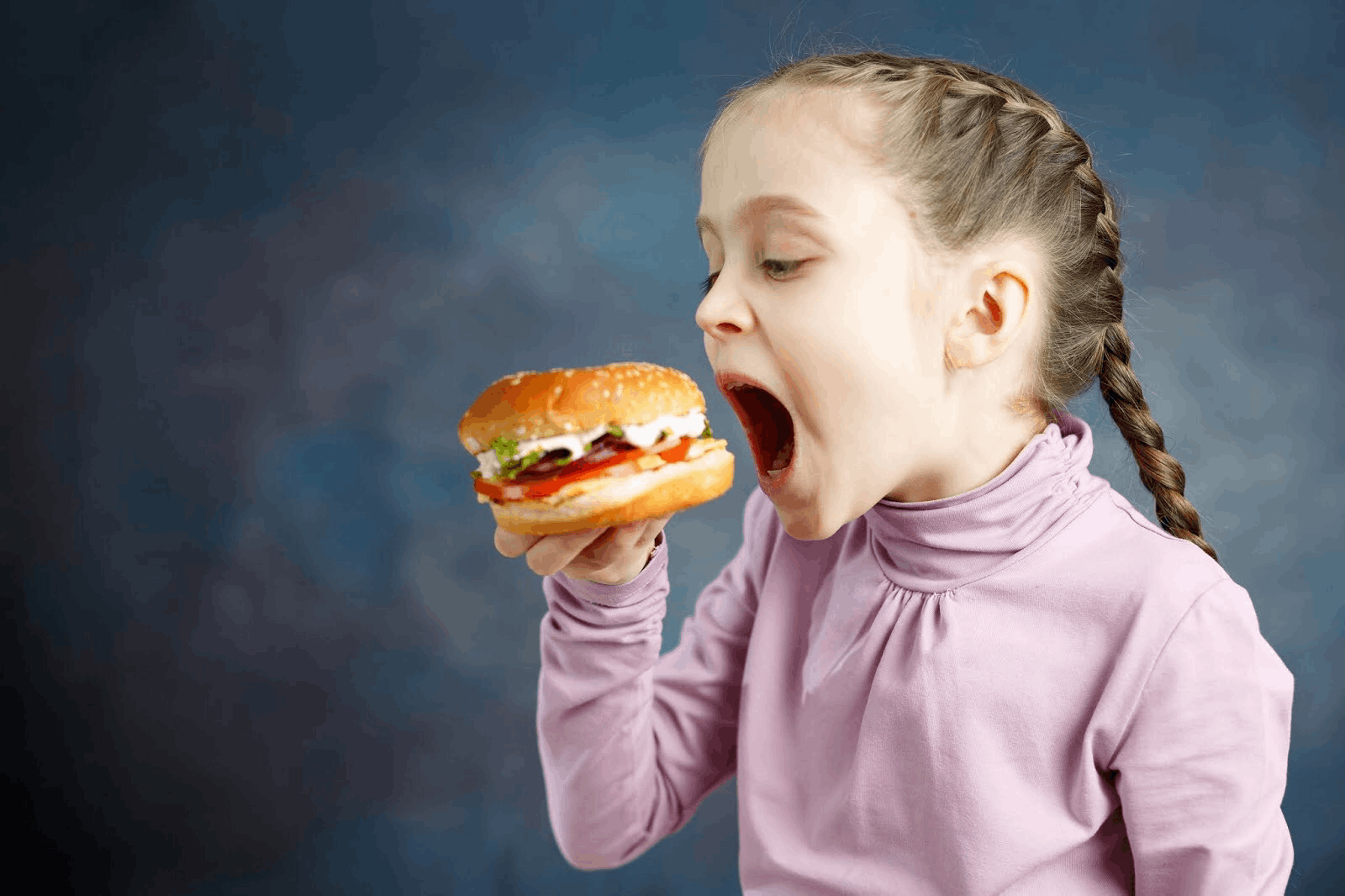 Держит еду во рту. Девочка ест бургер. Ребенок с бургером. Девочка с бургером. Ребенок ест чизбургер.